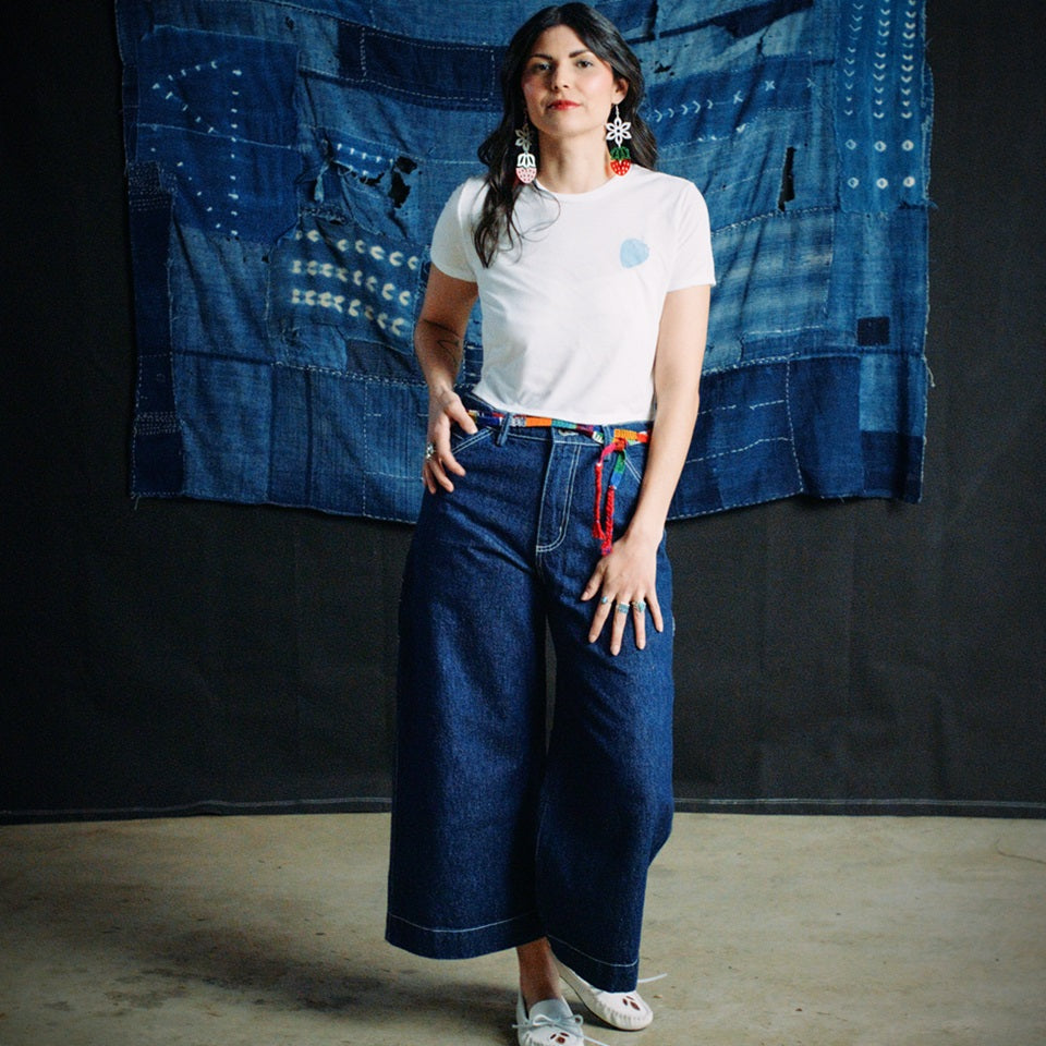 Native American model wearing indigo carpenter cropped pants and all cotton white tee with blue strawberry in upper left of shirt
