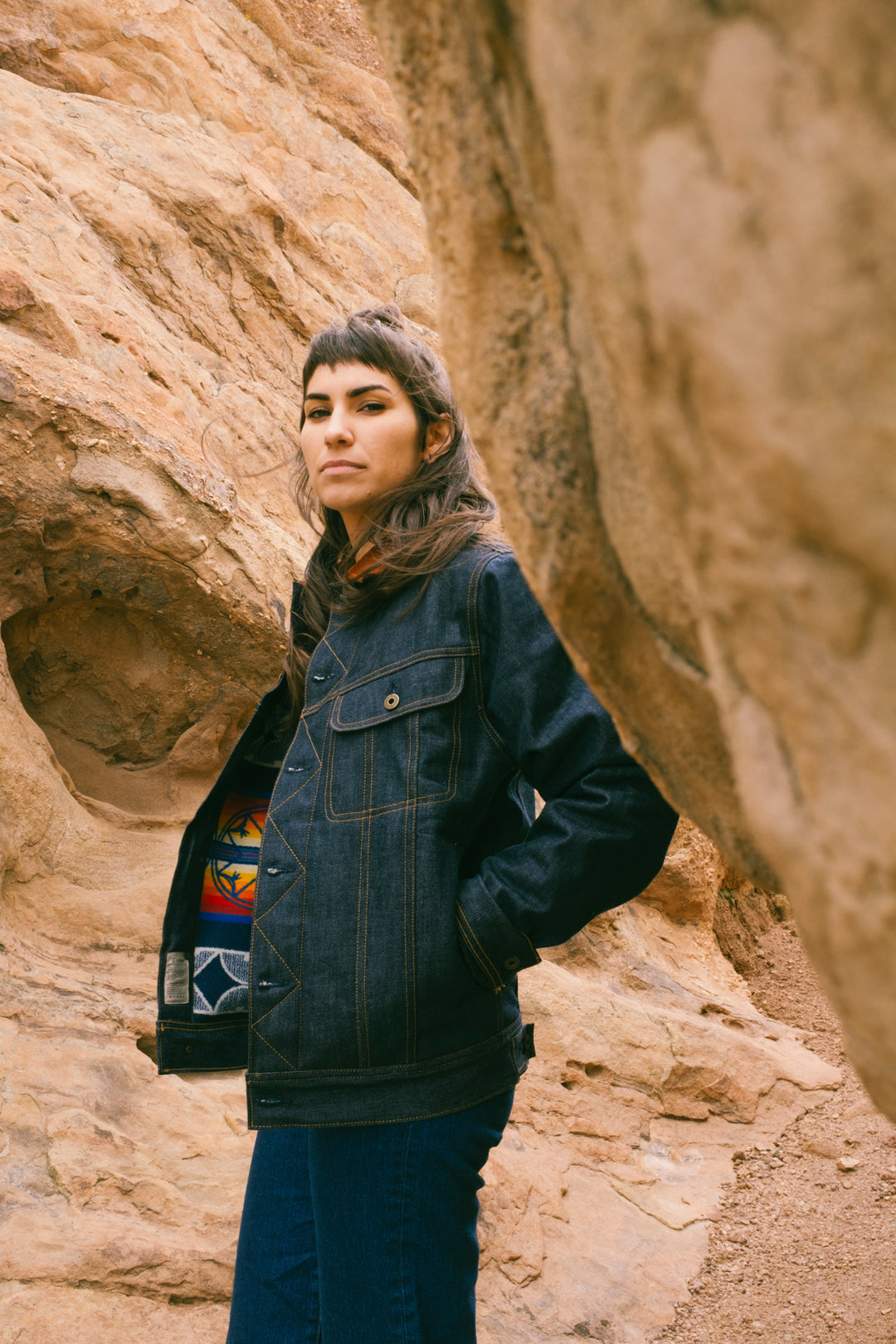 woman wearing denim jacket stands near rock formations