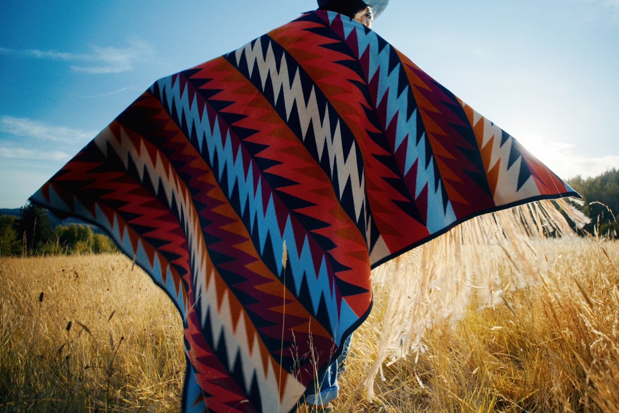 Red, black, tan wool blanket by Ginew and Native American model in field