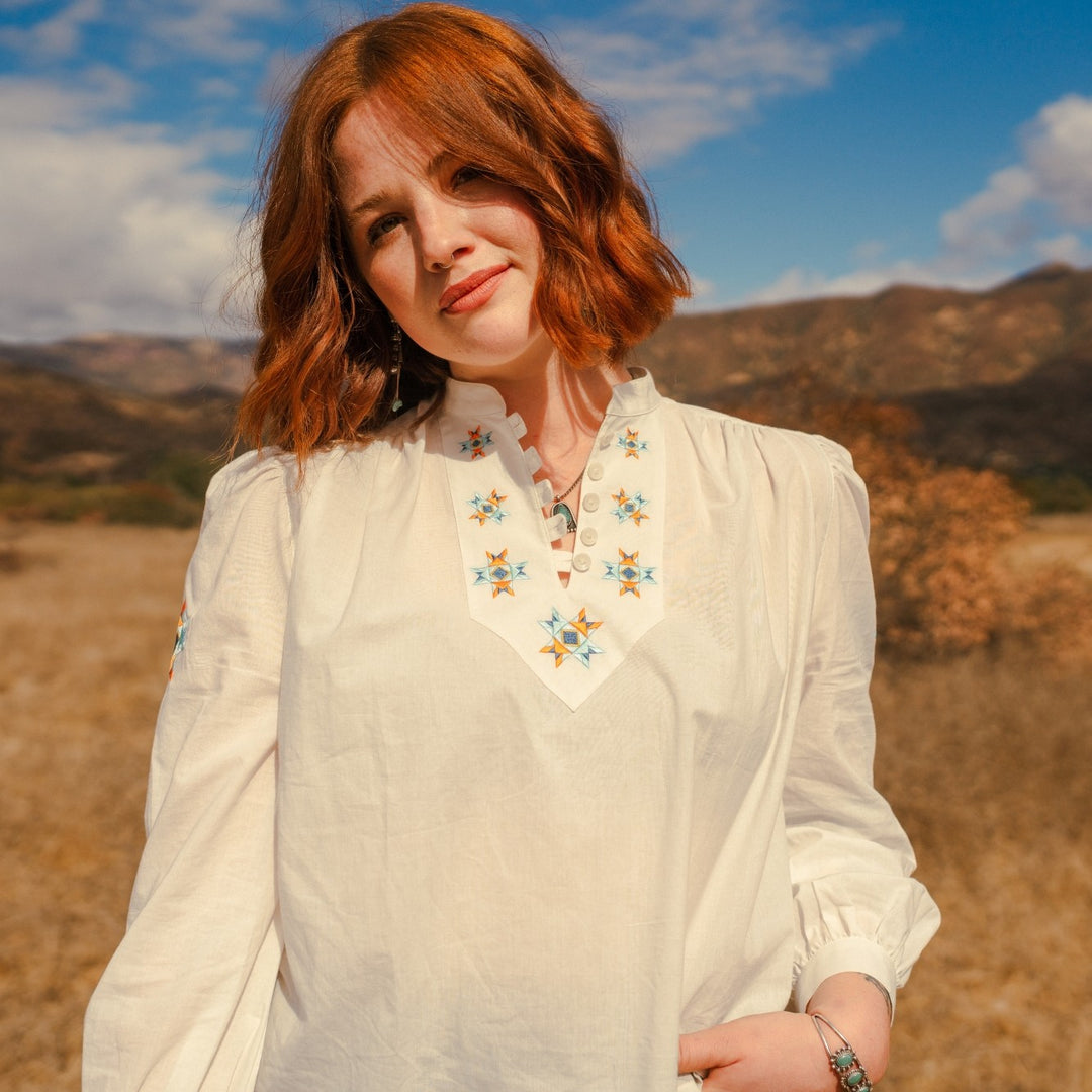 Close up of Woman wearing white peasant style white blouse with Native American embroidery of the star quilt design by Ginew