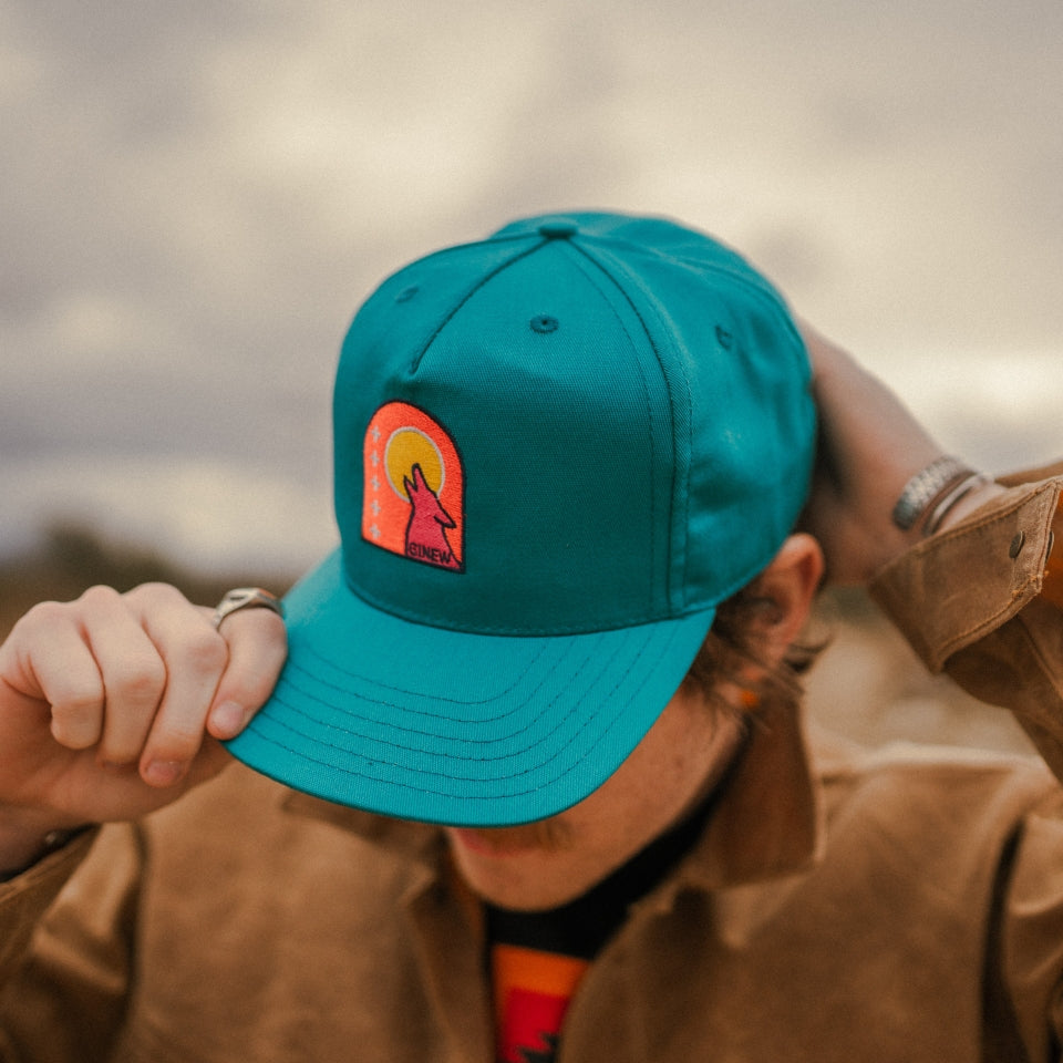 Close up of Coyote trucker hat with Ginew word in teal aqua blue and sunset colors 