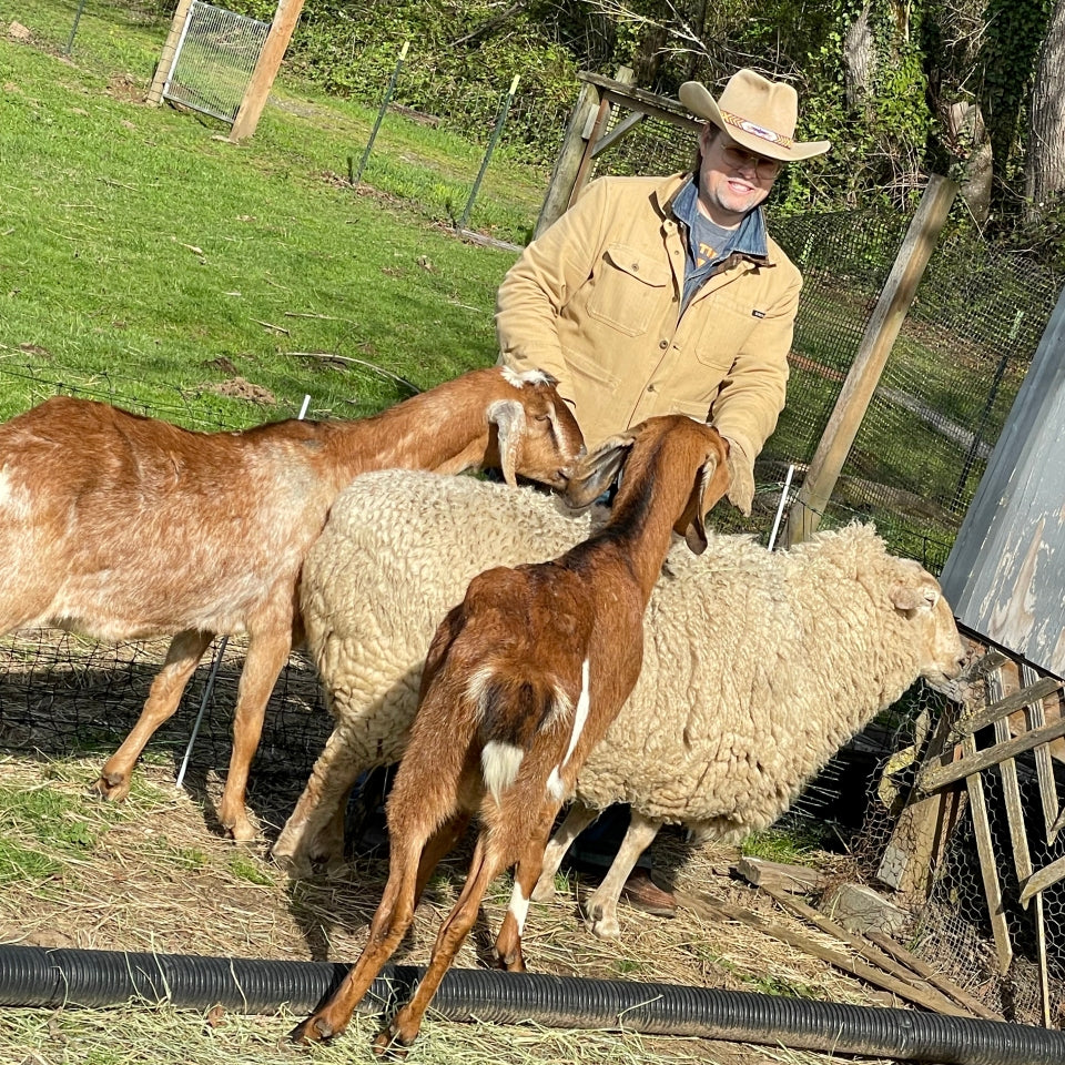 Native American Erik Brodt wearing tan saddle herringbone chore barn jacket surrounded by farm animals