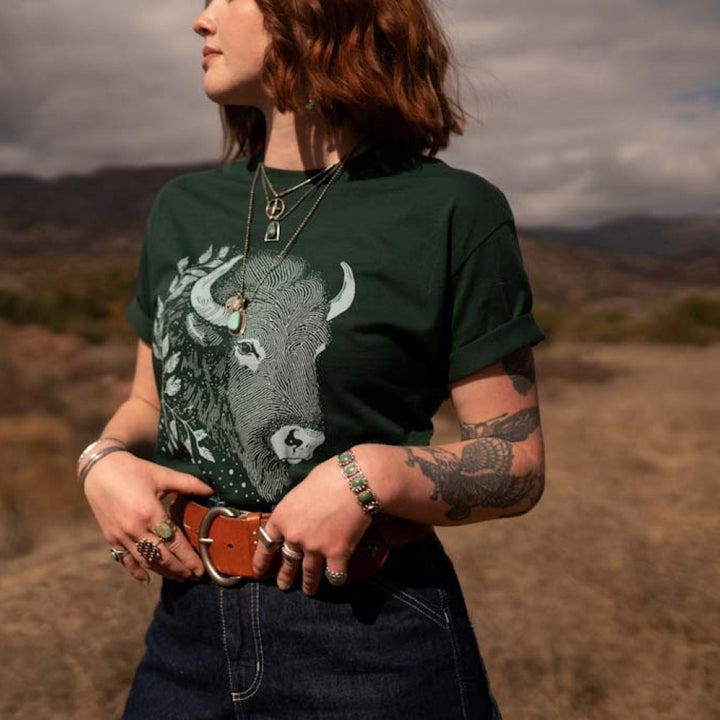 Woman wearing bison t-shirt in green standing in field 