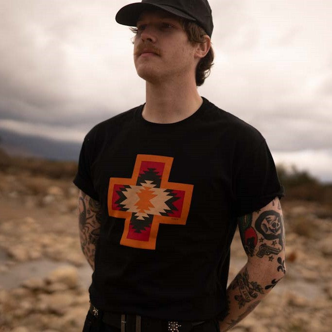 Man wearing Native American four direction t-shirt in black and orange and red with black wax canvas hat 