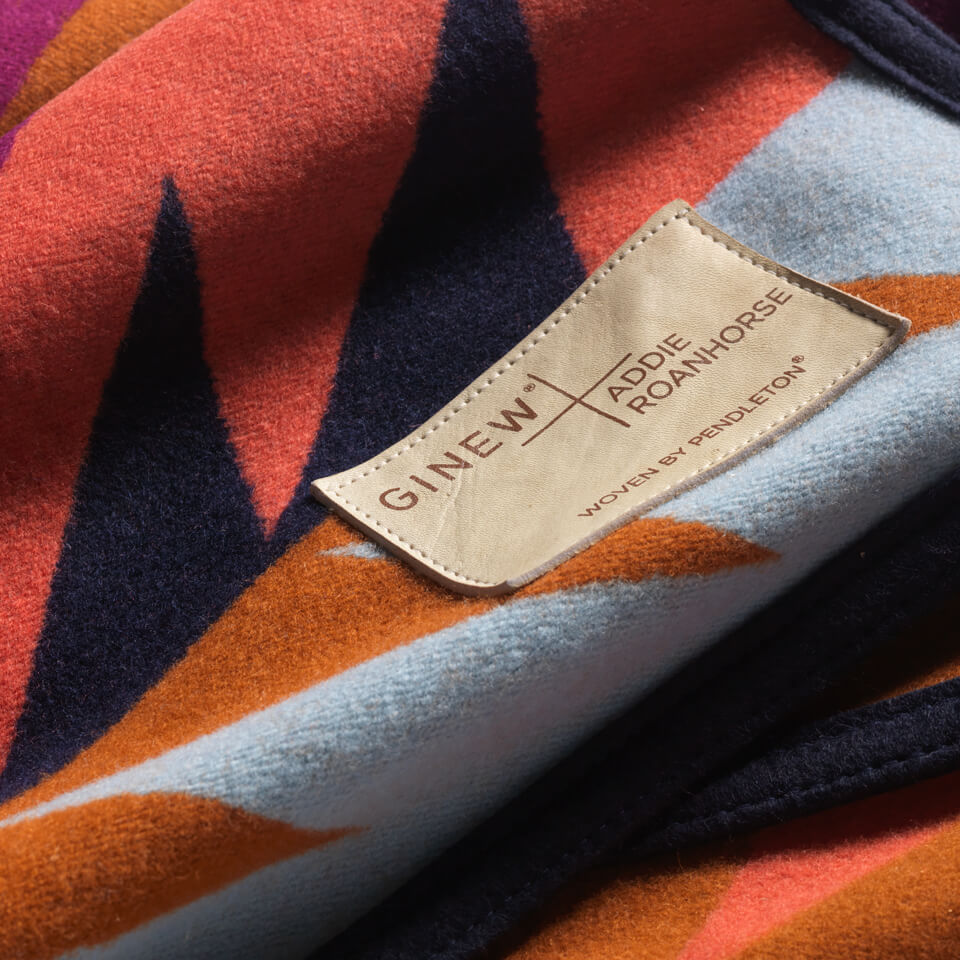Close up of 100% wool blanket in blue, brown, plum, black and tan made in USA with a leather label 