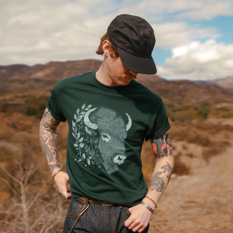 Man hiking wearing bison buffalo t-shirt and black wax canvas hat by Indigenous Ginew 