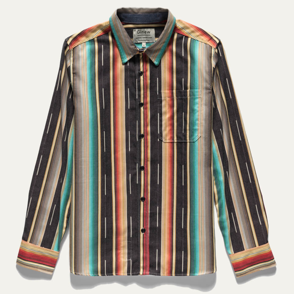 Mohican Stripe Shirt on white background. Shirt is a button up and features multiple colored vertical stripes (black, white, turquoise, yellow, red, brown, cream). Shirt lay on a white background.