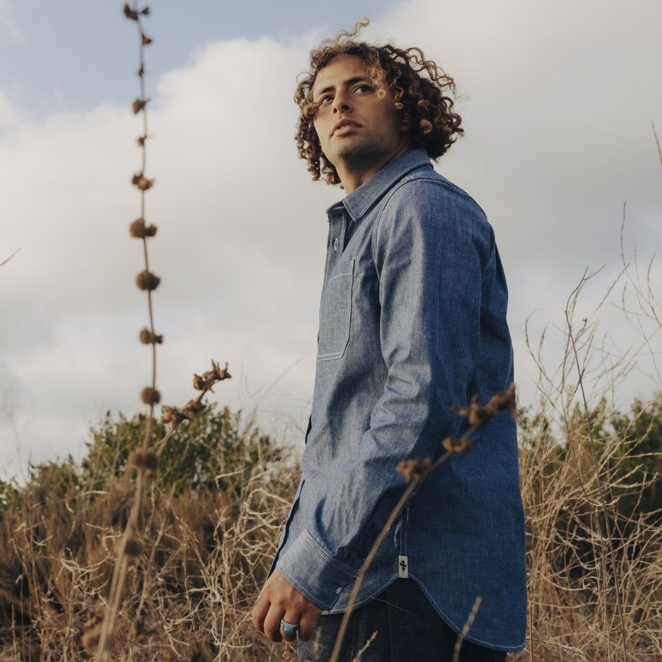 Male wearing blue chambray button down shirt in all cotton with Ginew oak leaf at bottom seam