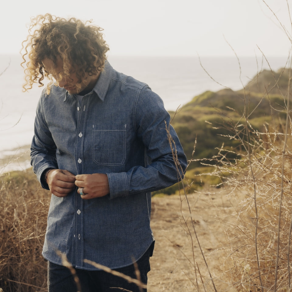 Front of Male wearing blue chambray button down shirt in all cotton with Ginew oak leaf at bottom seam