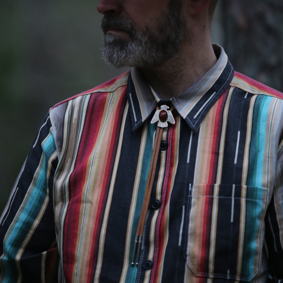 All Cotton striped button down in blue red black and tan on male model in woods