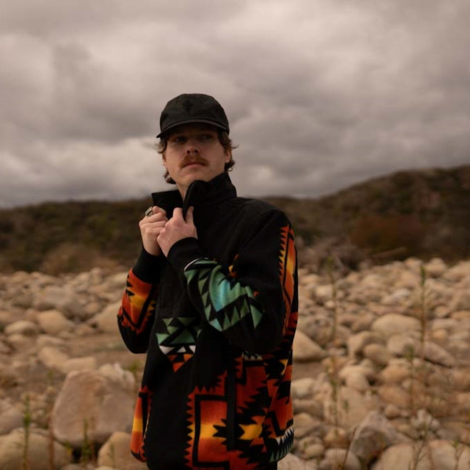 Man in field wearing a Black popover pullover half zip jacket with Native Americana fleece design from Indigenous Ginew