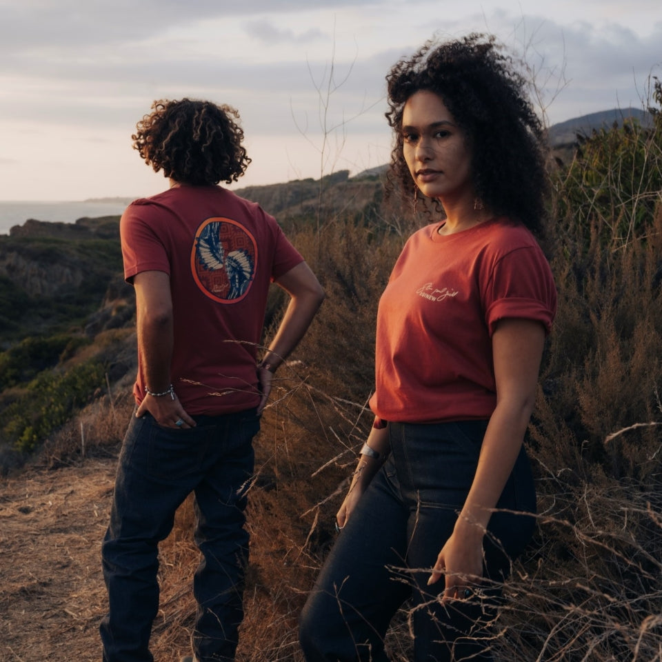 Male and female wearing Sitting Bull t-shirt in red maroon with Steven Paul Judd signature on front chest and Ginew