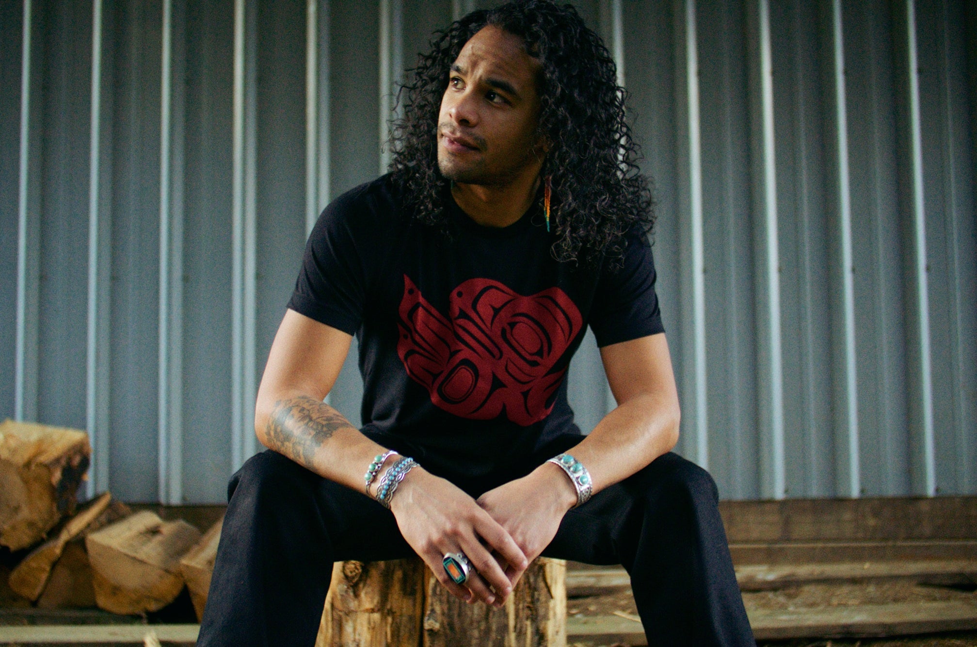 Native American Ginew Raven tshirt in red and black on model sitting outside