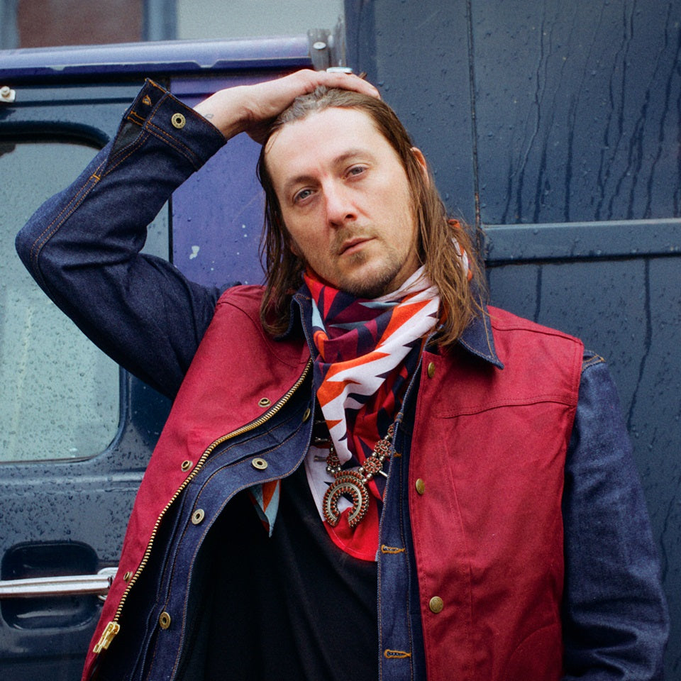 Red wax canvas vest over denim jacket on male model with colorful wild rag bandana