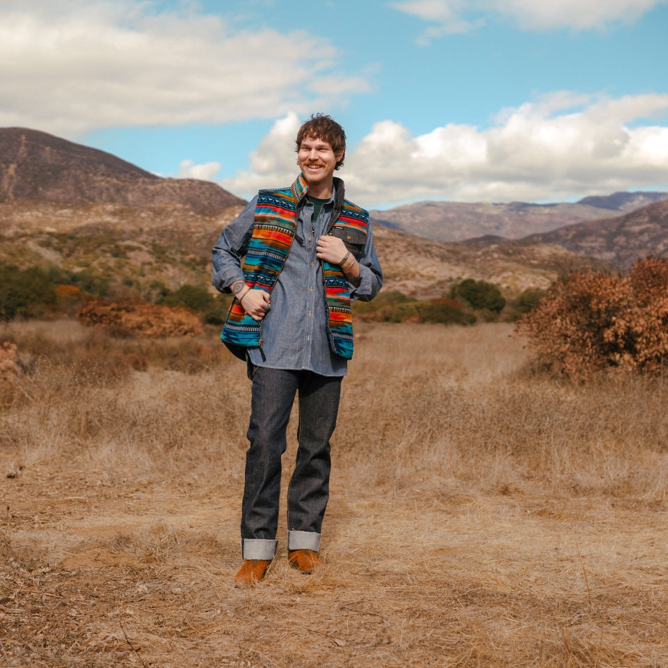 Man in canyon wearing denim reversible vest with printed fleece side showing made by Indigenous Ginew