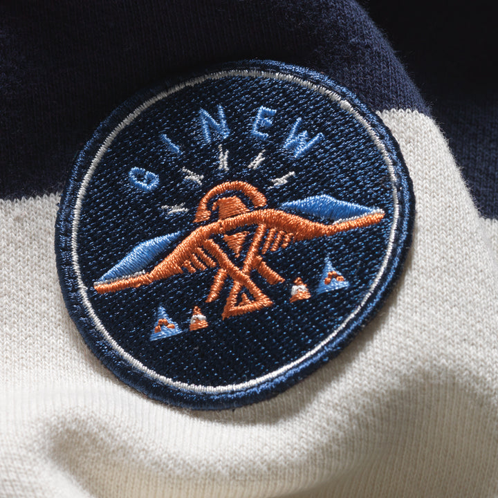 Close up of embroidered Thunderbird patch in blue and copper on Navy and off white rugby shirt made by Native American Ginew