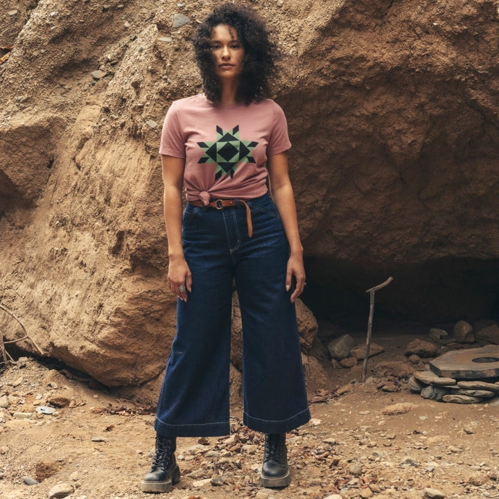 Woman wearing cropped denim carpenter pants and mauve t-shirt with Native American star icon in black and green star quilt design