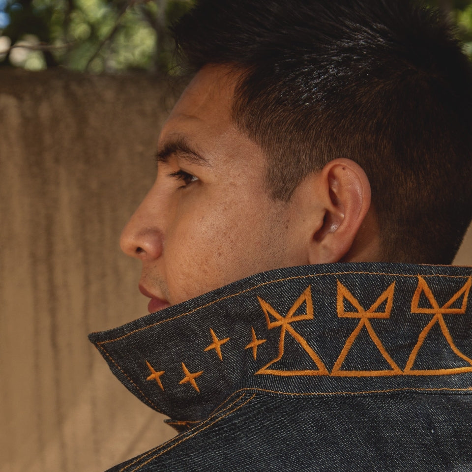 Close-up of a Native American wearing a denim jacket with embroidered details, looking away from the camera.