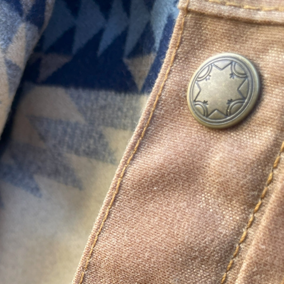 Button close up on Women's brown wax canvas coat with colorful, southwest Pendleton wool lining with Native American Ginew tag