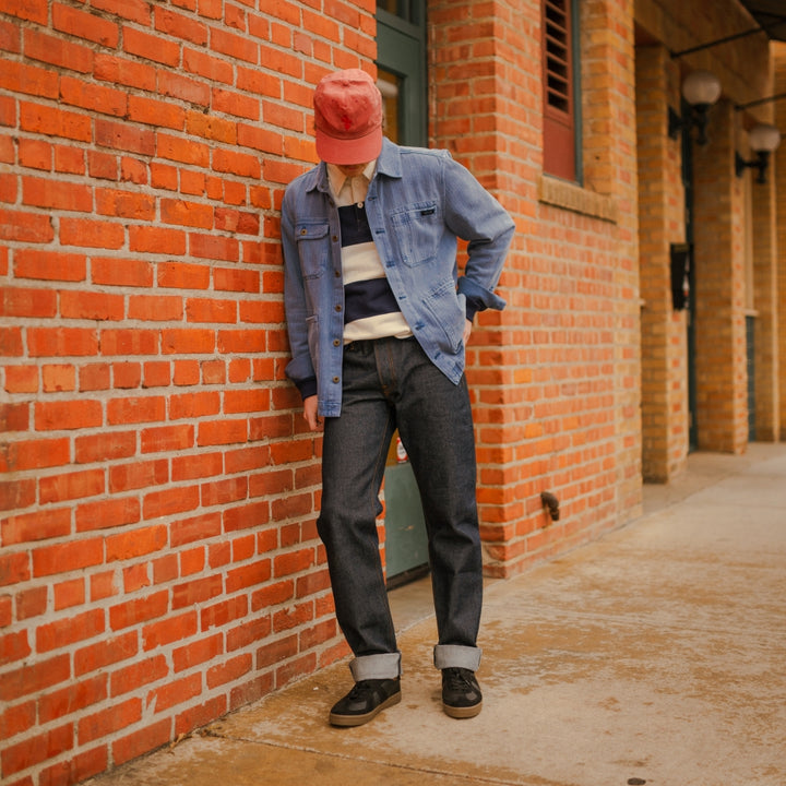 Man wearing blue barn jacket with stripe rugby leaning against wall 