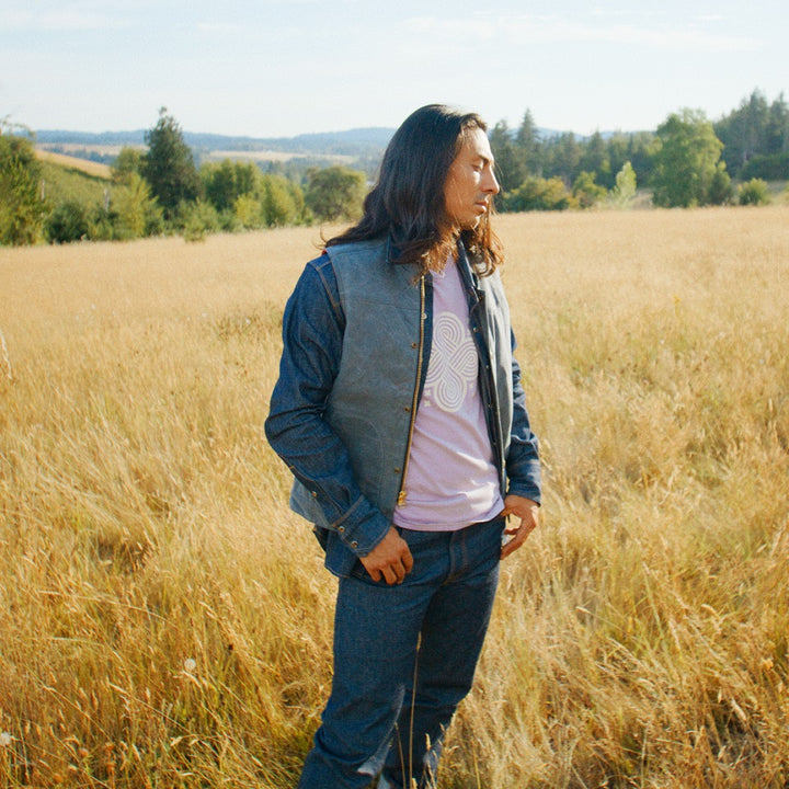 Native American wearing made in USA tshirt, wax canvas vest and selvedge denim jeans in field.