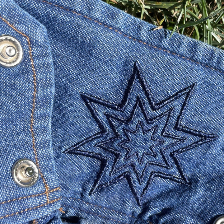 Close-up of a blue chambray denim like fabric with a 8 point Native American star-shaped embroidered design.