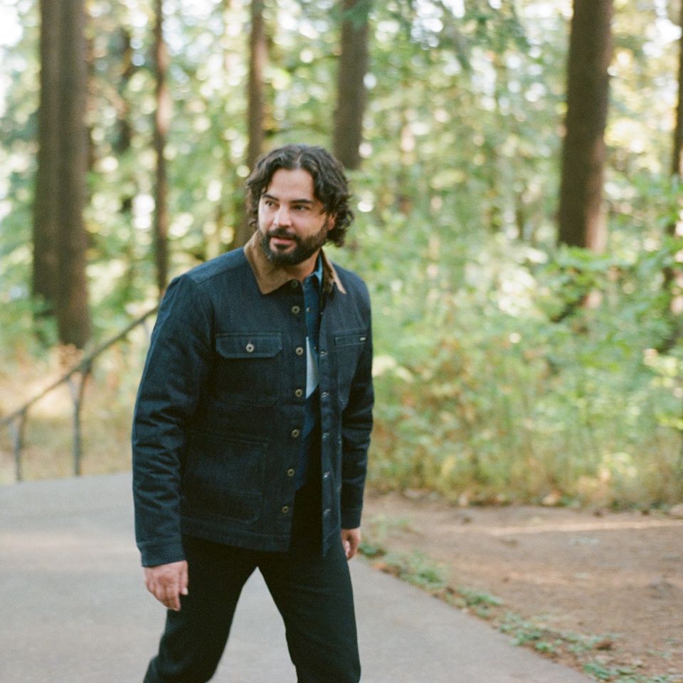 Man walking on a path in a forest wearing a dark denim jacket.