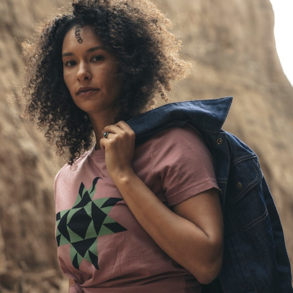 Woman wearing mauve t-shirt with Native American star icon on front in black and green 