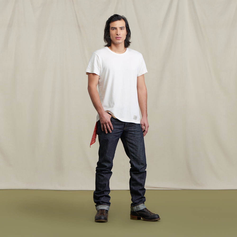 Native American male model wearing selvedge denim jeans and a white Tee with brown boots. Tshirt has a visible Ginew tag that reads Made in USA