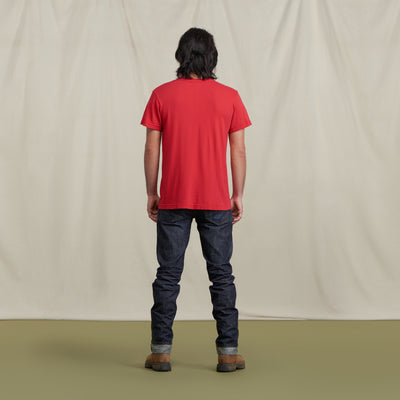 The picture is of a male model turned to the back wearing the Crew Tee Urban Red with jeans and brown boots. He is posed in front of a neutral background.