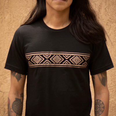 The picture shows a close-up of a man wearing the black Diamond Basket Tee printed with light brown ink. The man stands in front of a light brown background.