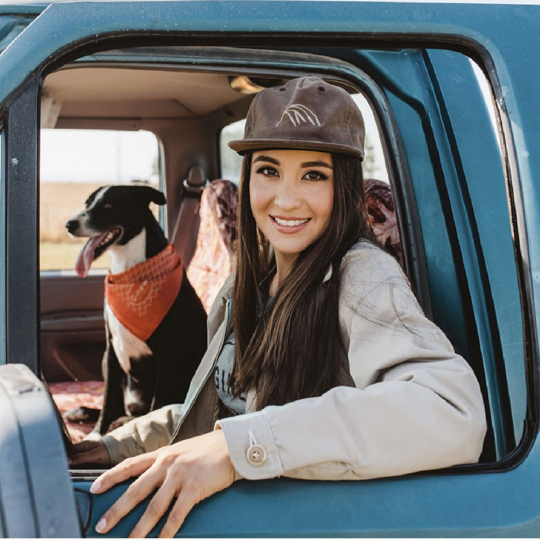 Woman in Crow Wing Ball Cap inside a blue pickup truck with a dog next to her.