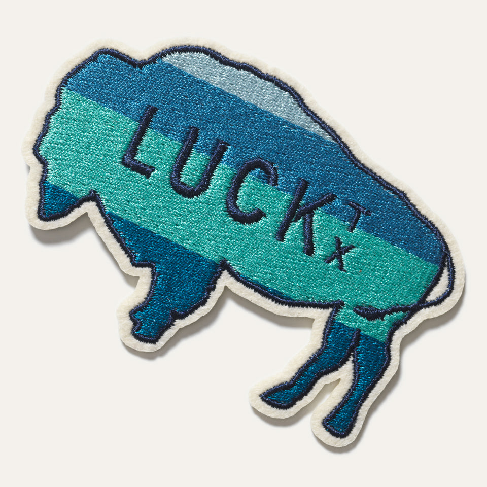 embroidered patch in the shape of a buffalo. outline of buffalo is navy and the words Luck TX in navy, with the background navy and mint. the embroidery is sewn on cream-colored scrim fabric