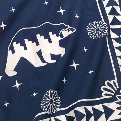 Close up of the center of the Bandana. Has a navy background and a side view of a Bear in the center in a cream color and is wearing glasses.