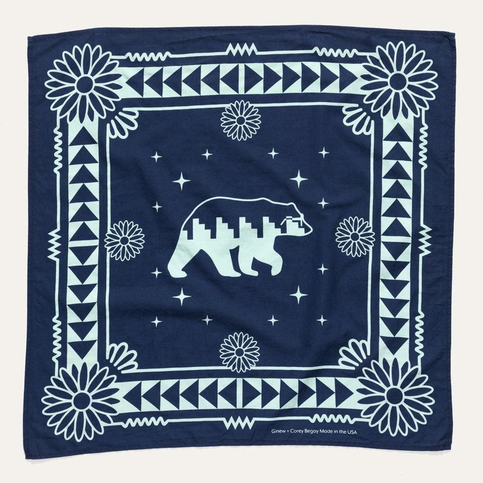 Full view of Naasgó Bandana which is navy and features a sky turquoise colored pattern around the borders and a side view of a bear in the center.