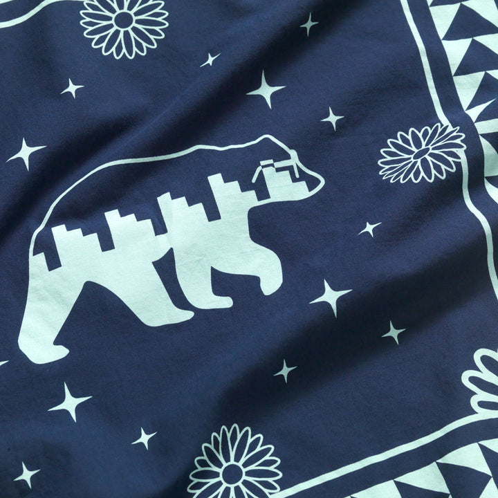 Close up of the center of the Bandana. Has a navy background and a side view of a Bear in the center in a sky turquoise color and is wearing glasses.