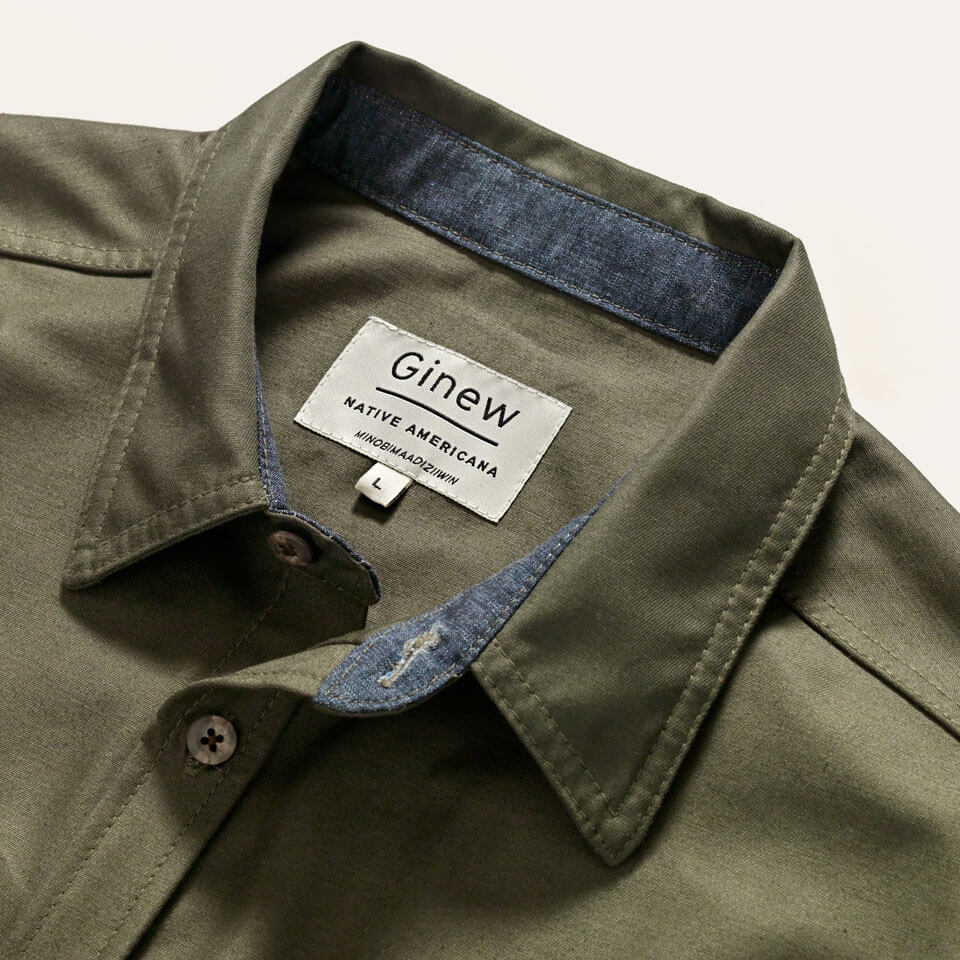 100% cotton, made in USA green shirt with a chambray contrast collar and interior tag reads Ginew, Native America. 