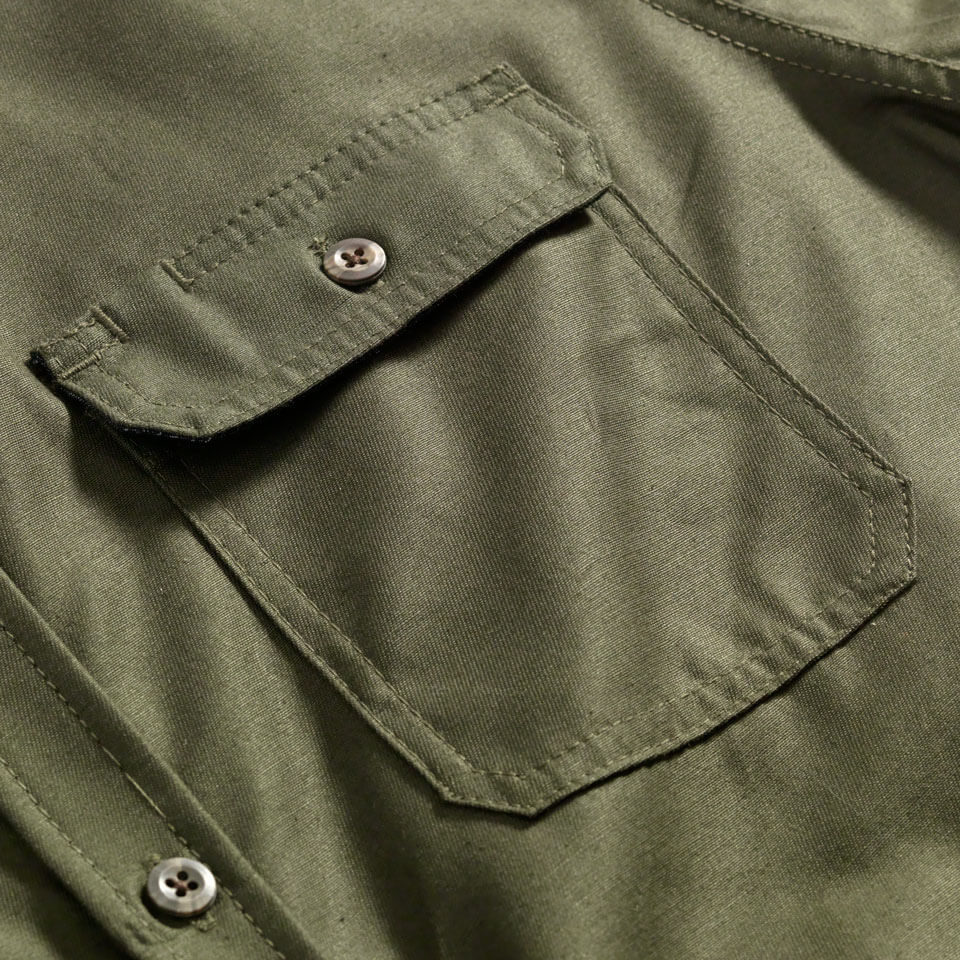 A close-up of an Army green button up Utility Shirt pocket with a button flap. Pocket has a notch for pen or sunglasses.