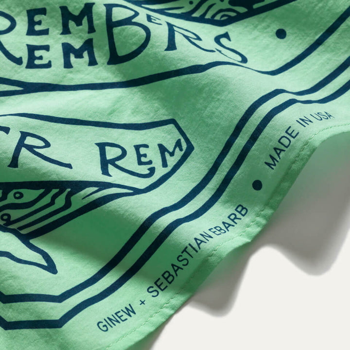 Mint green bandana with navy screen printing design with the words "water remembers" and fish. Rolled edge reads Ginew + Sebastian Ebarb, Made in USA