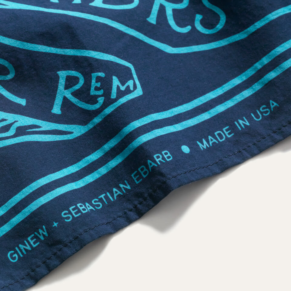 Navy bandana with aqua blue screen printing design with the words "water remembers" and fish. Rolled edge reads Ginew + Sebastian Ebarb, Made in USA