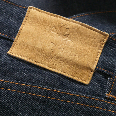 Selvedge denim jean. Close up of Hunted Deer Skin Leather Patch (Ojibwe Territory) on top backside (by the belt loops) of jean.