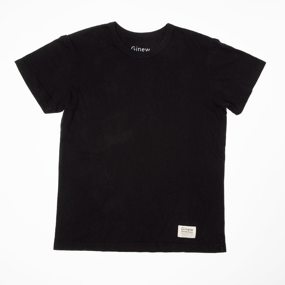A crew t-shirt in a jet black color is laid flat on a white background. The shirt has a white tag at the bottom left hem with the word Ginew on it.