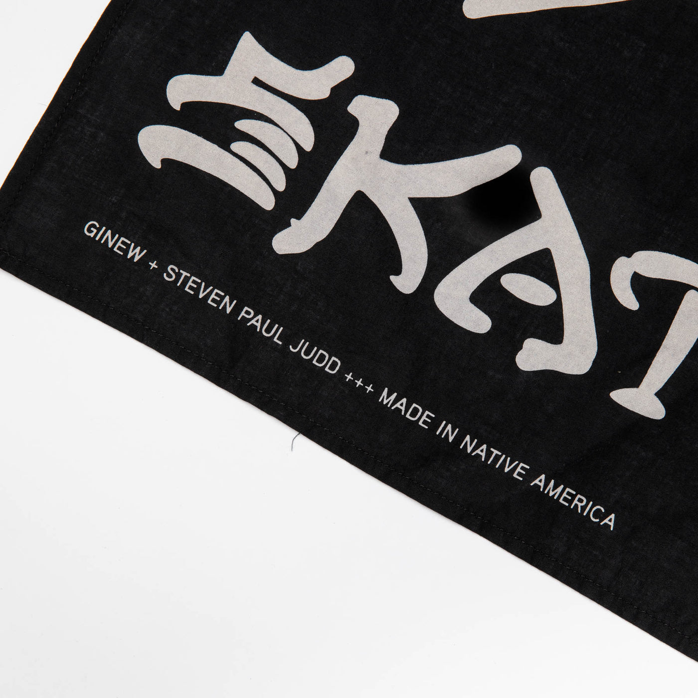 close up of the bottom left corner of the black bandana with off-white lettering that says "Ginew + Steven Paul Judd +++ Made in Native America"
