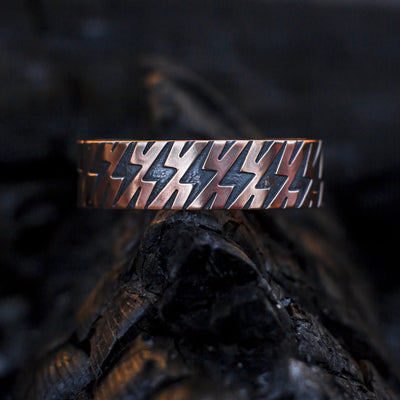 Solid copper bracelet with black patina and a lightning bolt pattern. Shown on a charcoal log.