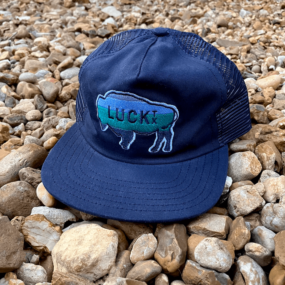 Navy blue trucker hat with embroidered buffalo patch set on beach of rocks