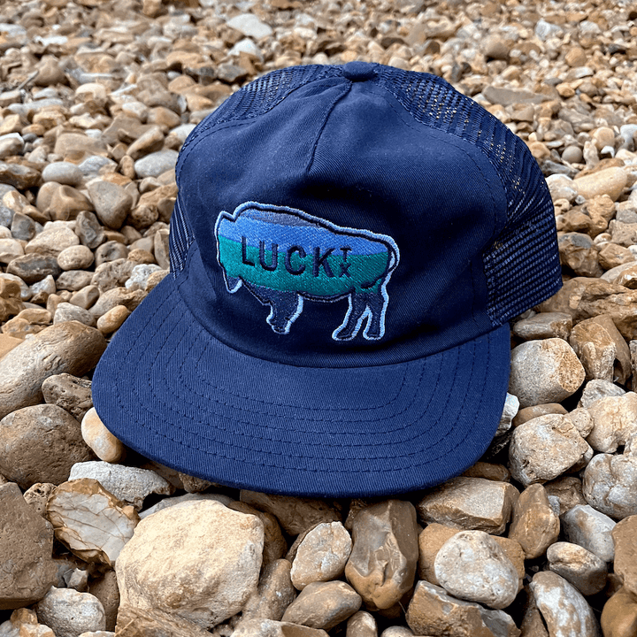 Navy blue trucker hat with embroidered buffalo patch set on beach of rocks